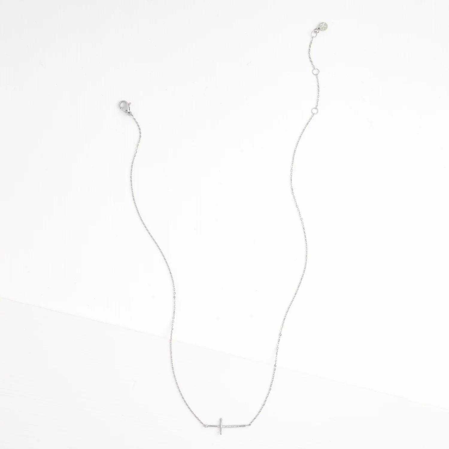 A delicate silver chain necklace with a small, minimalist cross pendant at the center, displayed against a clean white background.