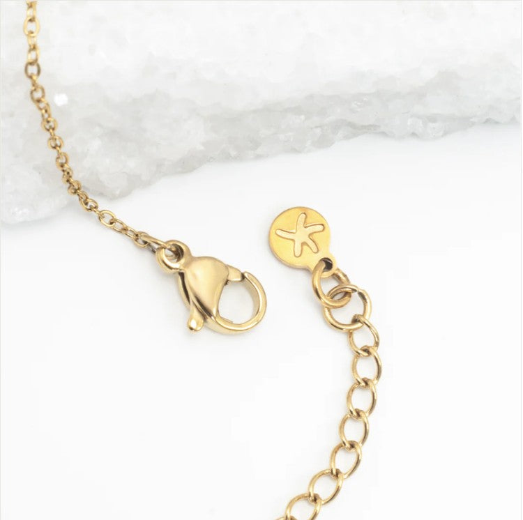 Close up photo of a gold necklace lobster clasp on a white marble background
