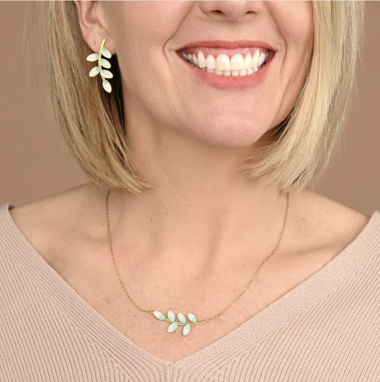 Woman wearing a matching gold necklace and earring set with leaf design on a beige background