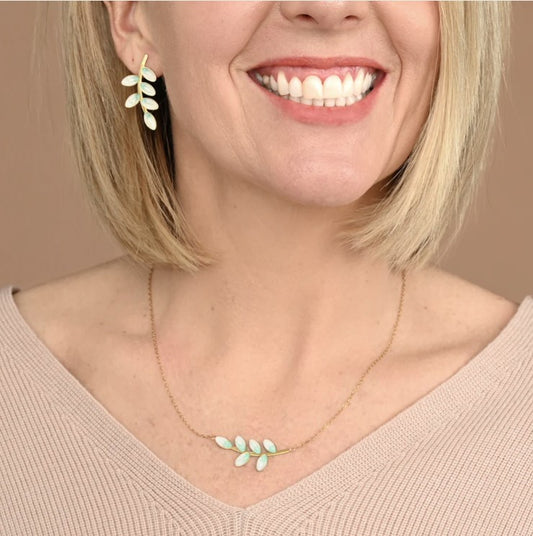 Woman wearing a matching gold necklace and earring set with leaf design on a beige background