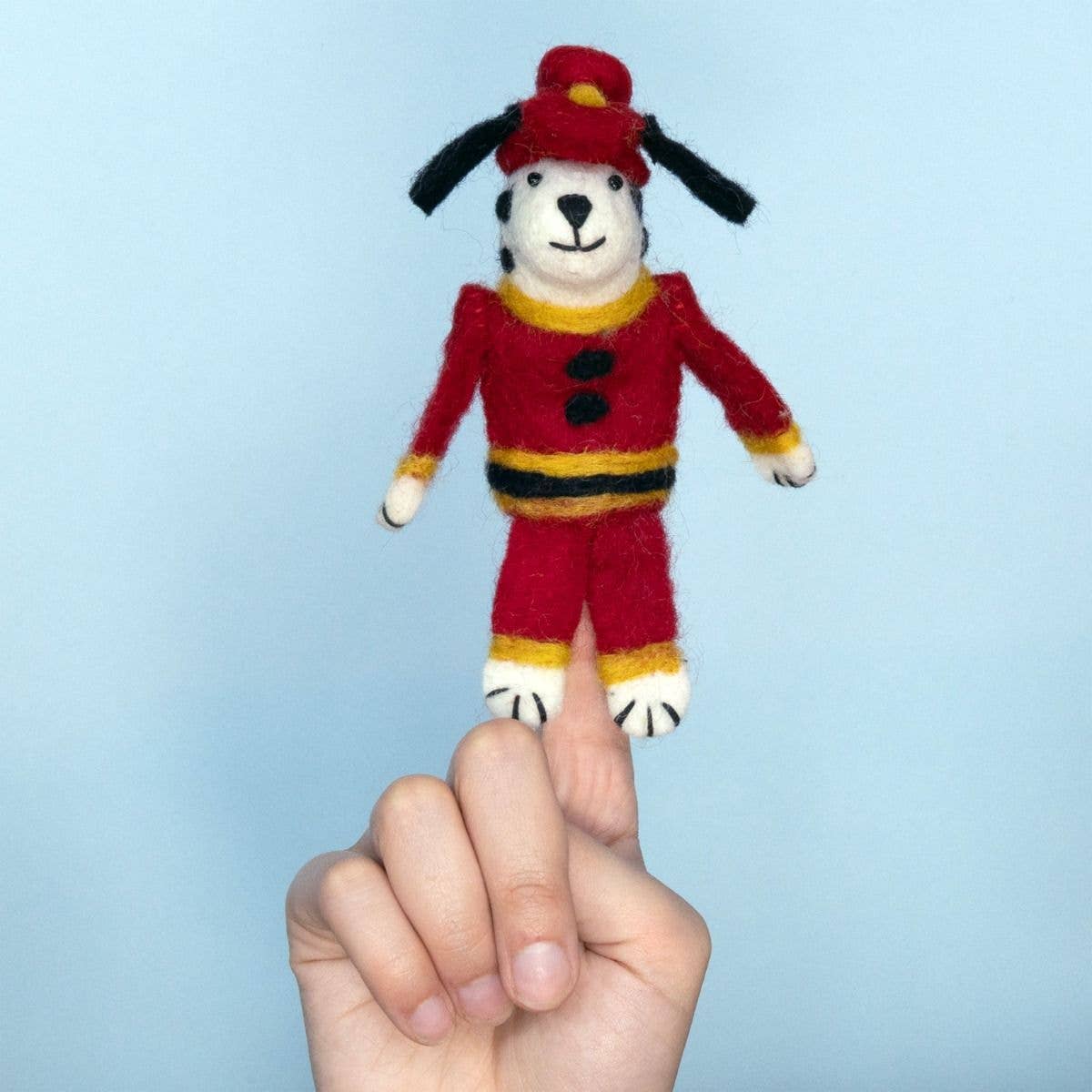 Hand holding a small felt dog toy dressed in a red outfit against a light blue background