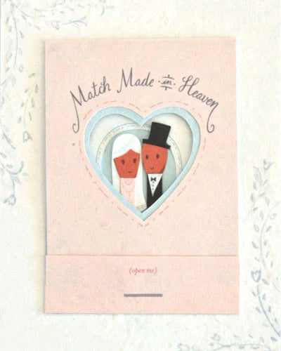 Greeting card with cut-out figures of a bride and groom inside a heart, on a light pink background.