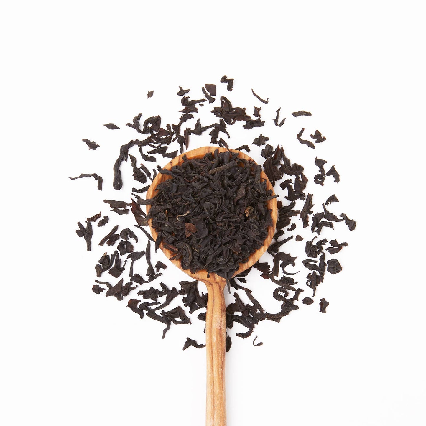 Wooden spoon filled with black tea leaves on a white background