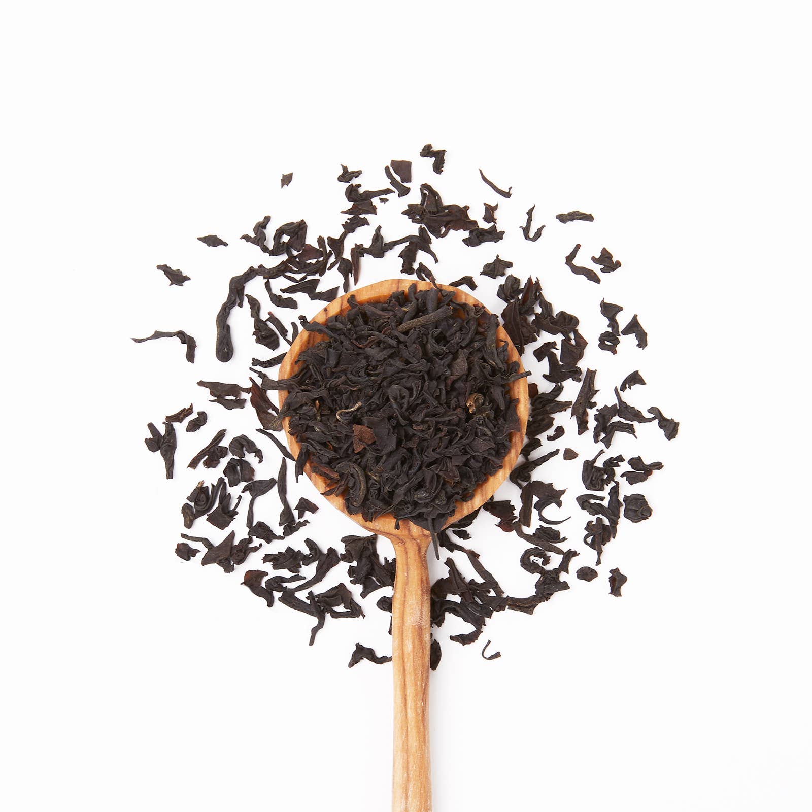 Wooden spoon filled with black tea leaves on a white background
