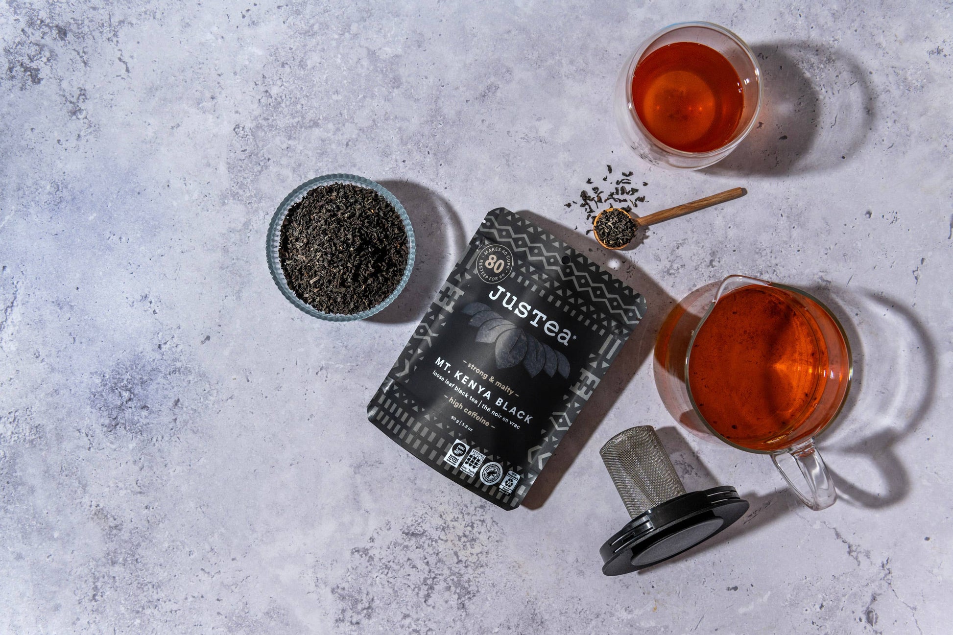 Justea tea packaging with two cups of tea on a gray surface