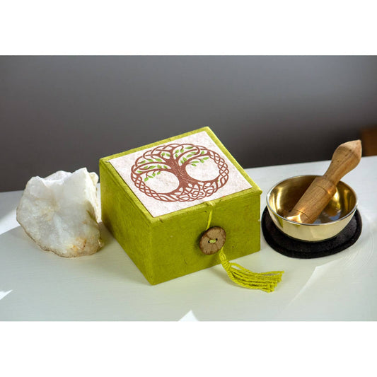 Green box with tree of life design, white stone, gold singing bowl with wooden striker on gray background