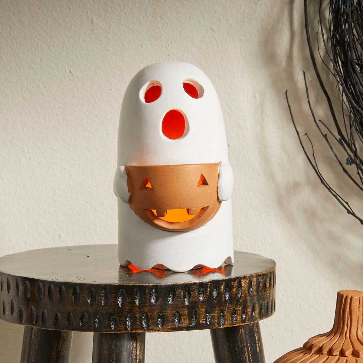 Terracotta lantern in the shape of a white ghost holding an orange jack o lantern on wooden stool