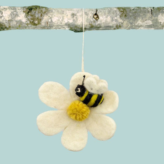 White daisy ornament with a bee hanging from a birch branch against a light blue background.