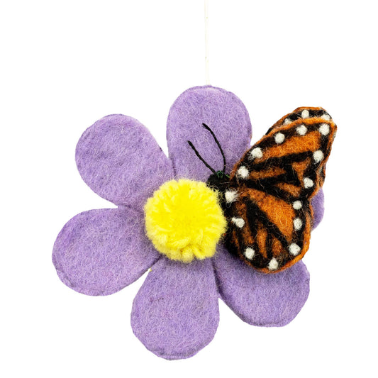 A felt flower ornament with six lavender-purple petals, a bright yellow pom-pom center, and a monarch butterfly applique resting on top, shown against a plain white background.