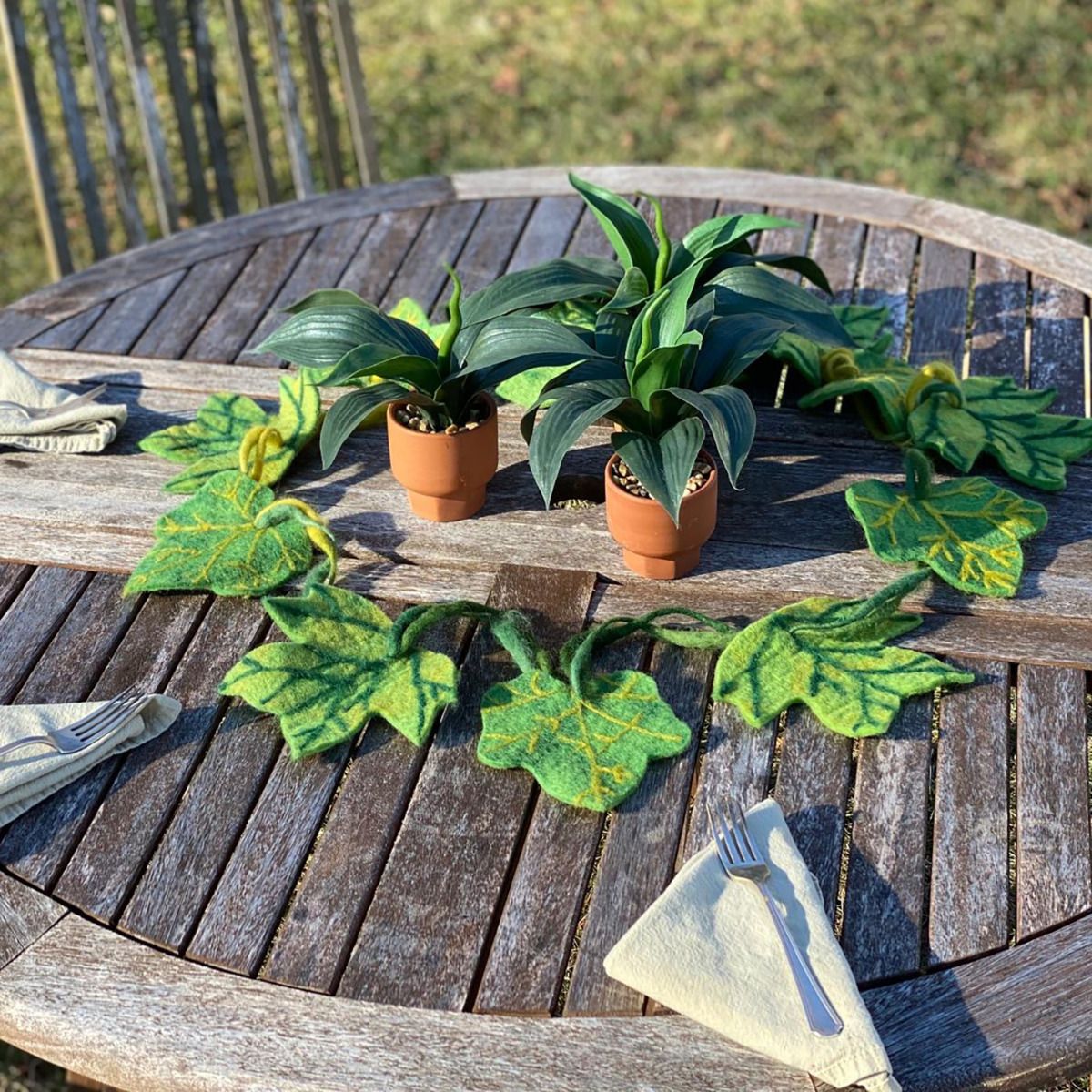 Green felted leaf garland on a wooden table with live plants