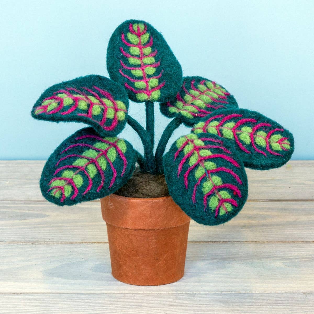 Felted potted plant with green and pink leaves on a wooden surface.