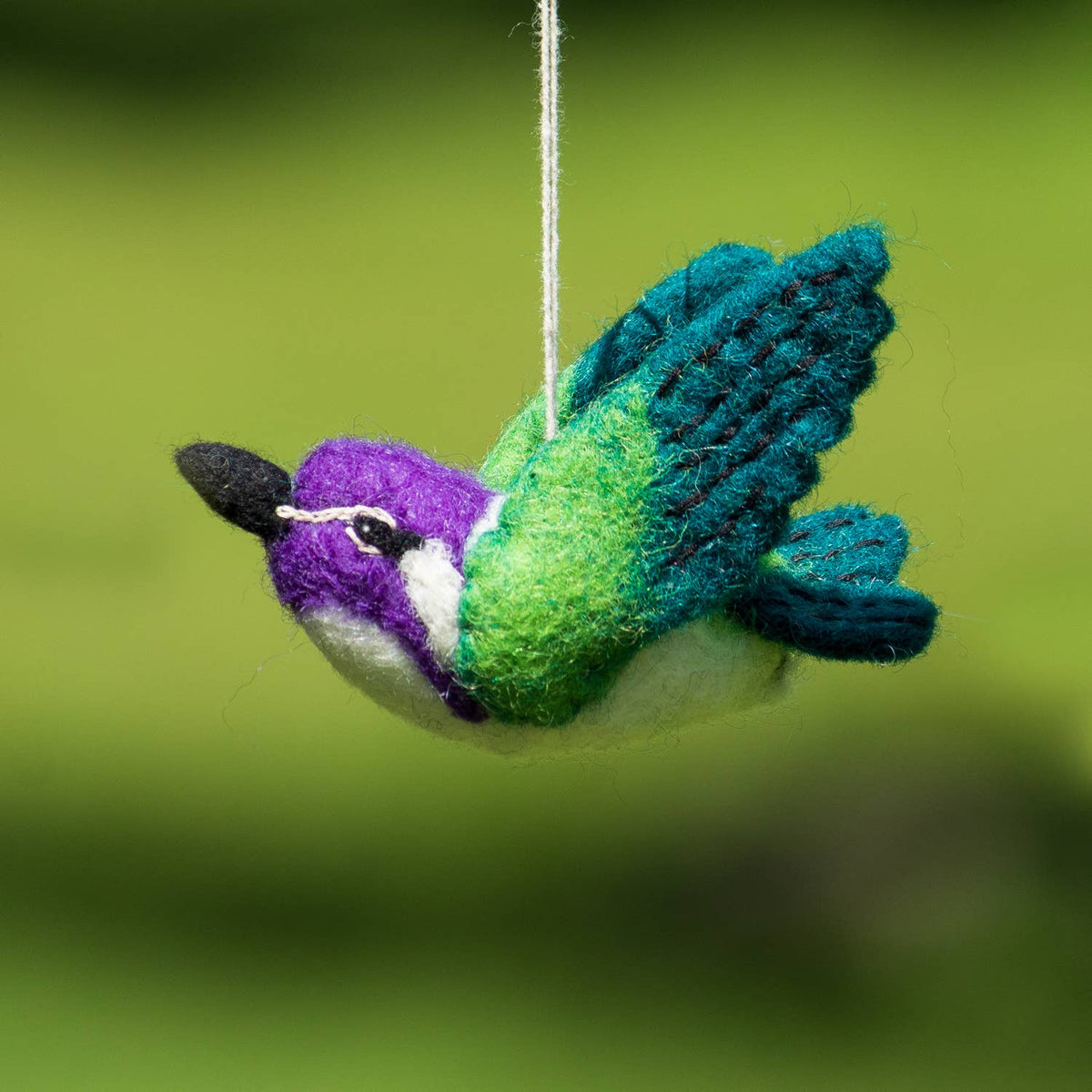 Felted green and purple hummingbird ornament hanging against a green background