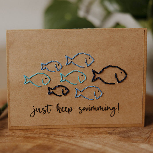 Card with embroidered fish and 'just keep swimming!' text on a brown recycled paper card.