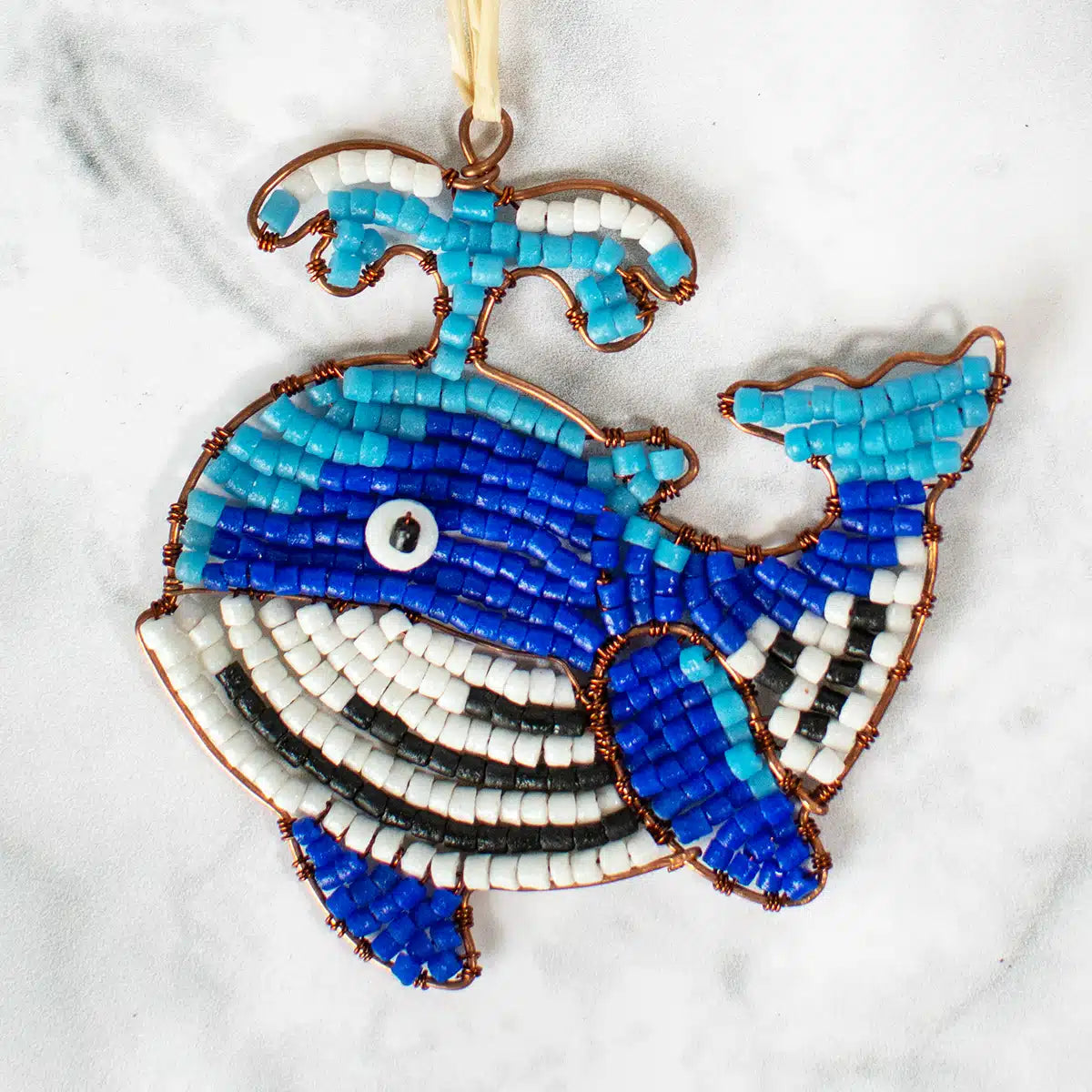 Blue and White whale shaped ornament made from glass beads and wired sits on a marble table.