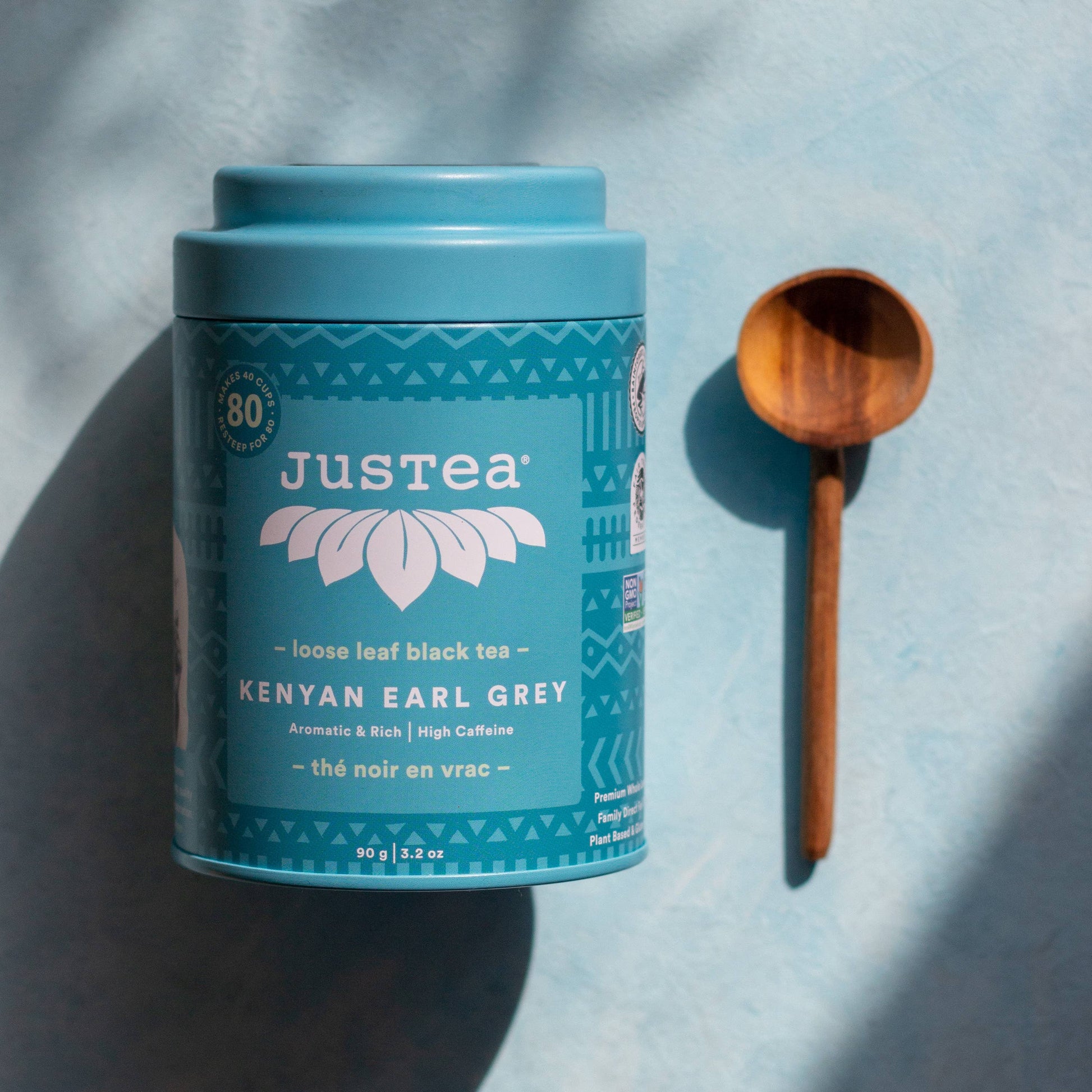 Justea Kenyan Earl Grey tea canister with a wooden spoon on a light blue background