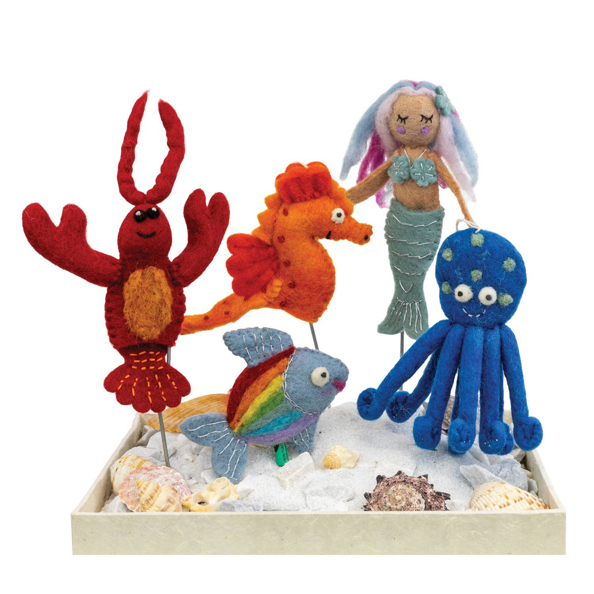 A set of colorful felt mermaid and sea life toys displayed in a tray with white faux sand and seashells on a white background. The set includes a red lobster, an orange seahorse, a mermaid doll, a blue octopus, a rainbow fish, and a small seashell toy.