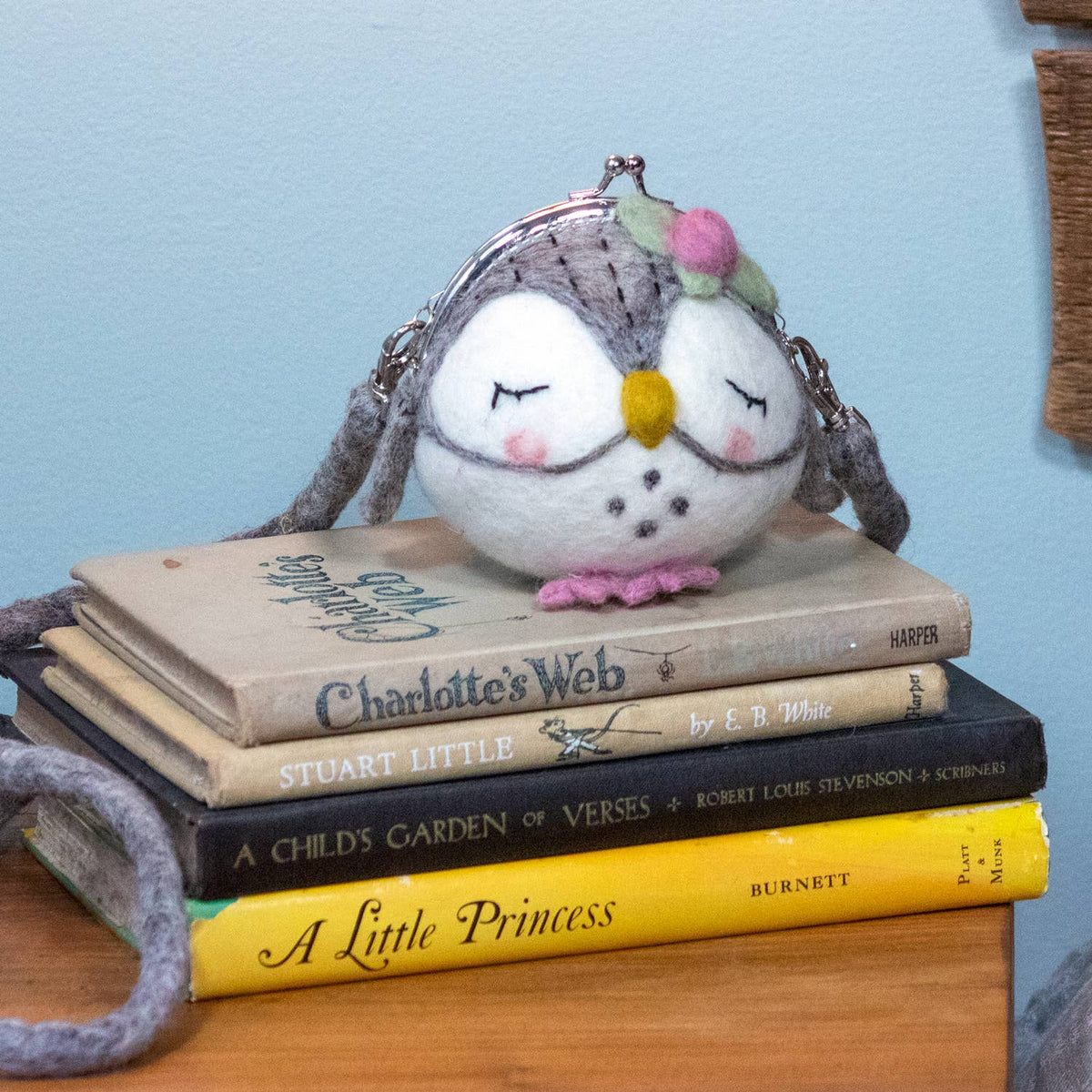 Owl-shaped handbag on a stack of books with a light blue background