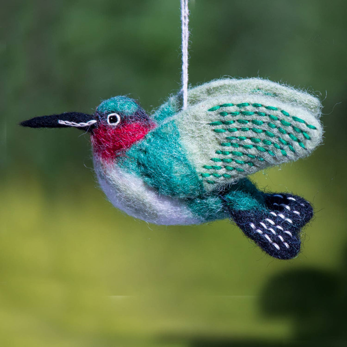 Decorative felt hummingbird ornament hanging against a blurred green background