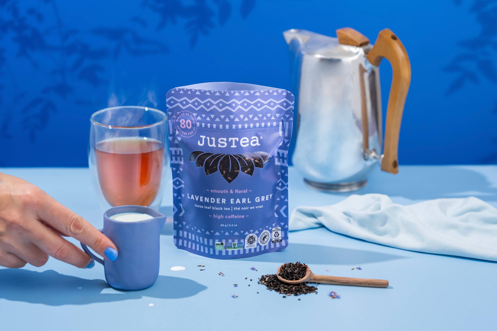 Tea-making setup with Justea lavender earl grey tea, a glass of tea, and a teapot on a blue background.
