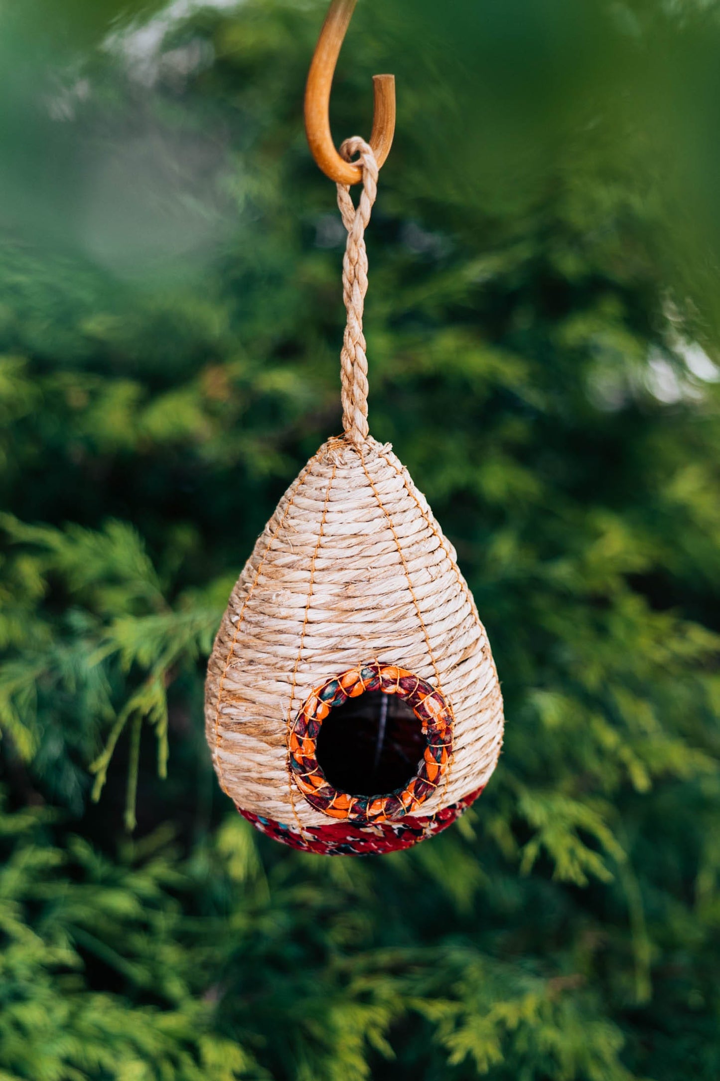 A teardrop-shaped birdhouse made from recycled cotton sari textiles and banana fiber, with a brown color and a multicolored pattern around the bottom.