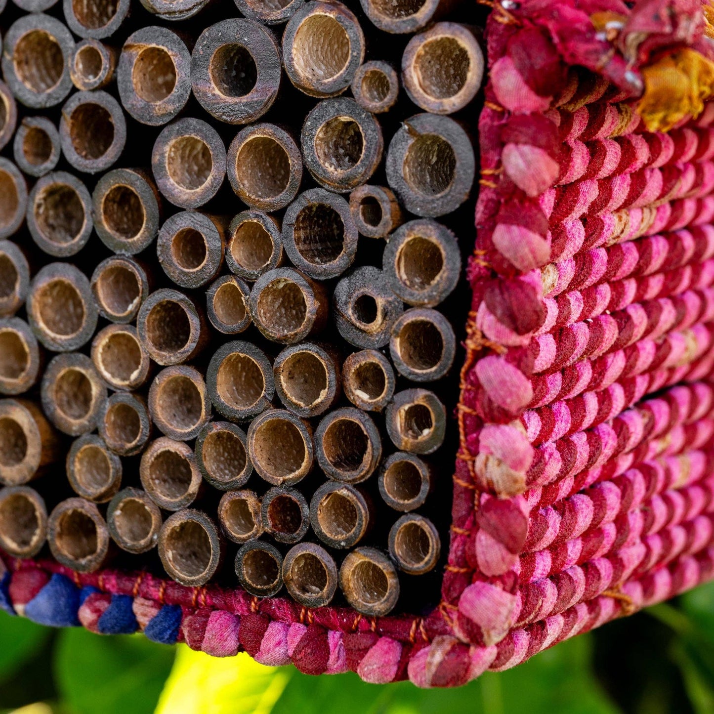 Close-up of stacked wooden beehive blocks with pink and blue fabric on a green background