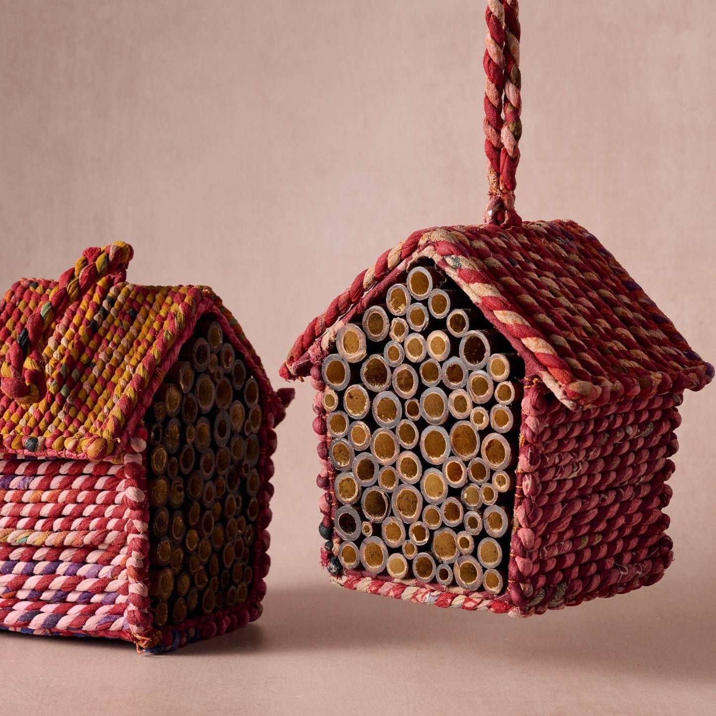 Two woven bee houses with colorful patterns on a beige background