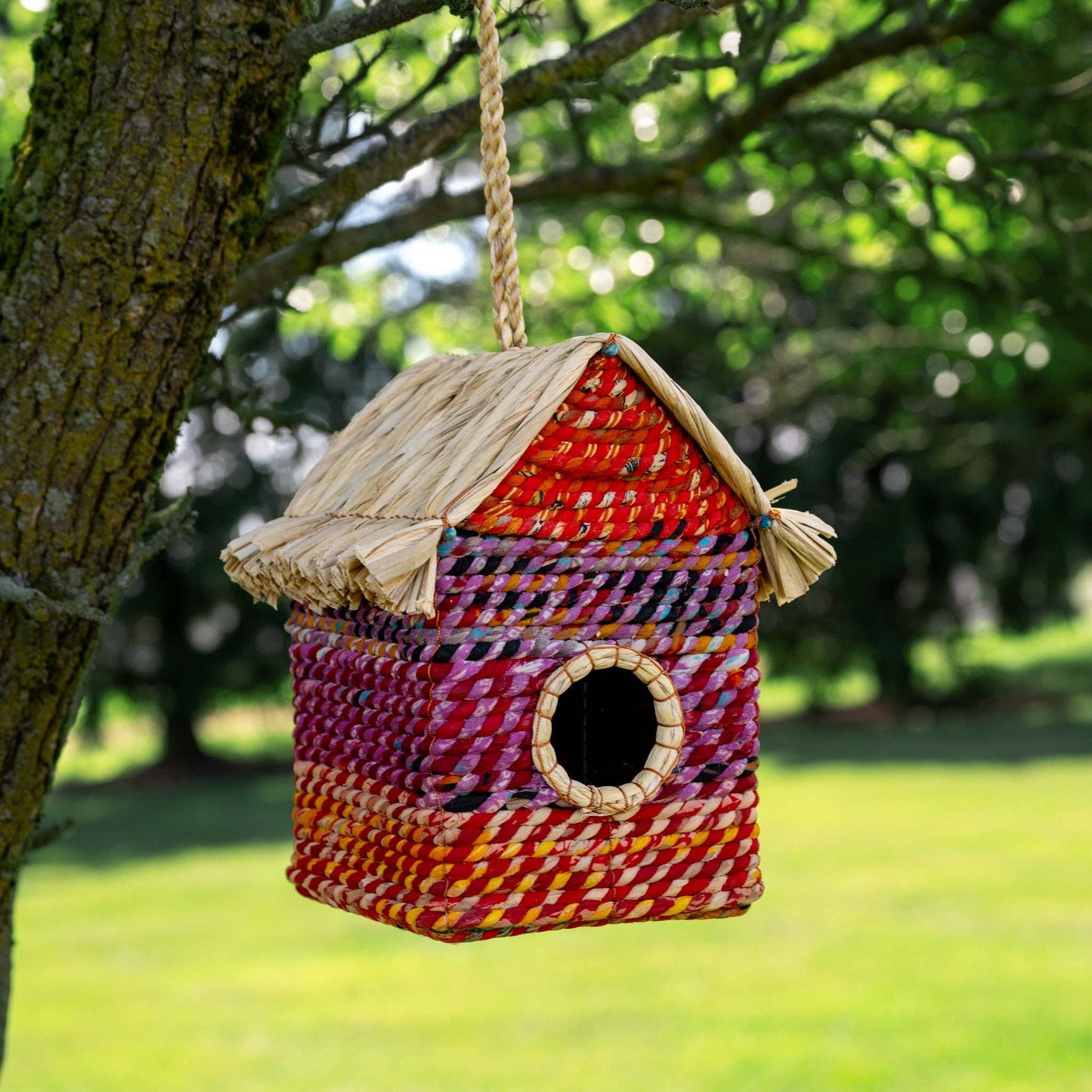 Colorful woven birdhouse hanging from a tree