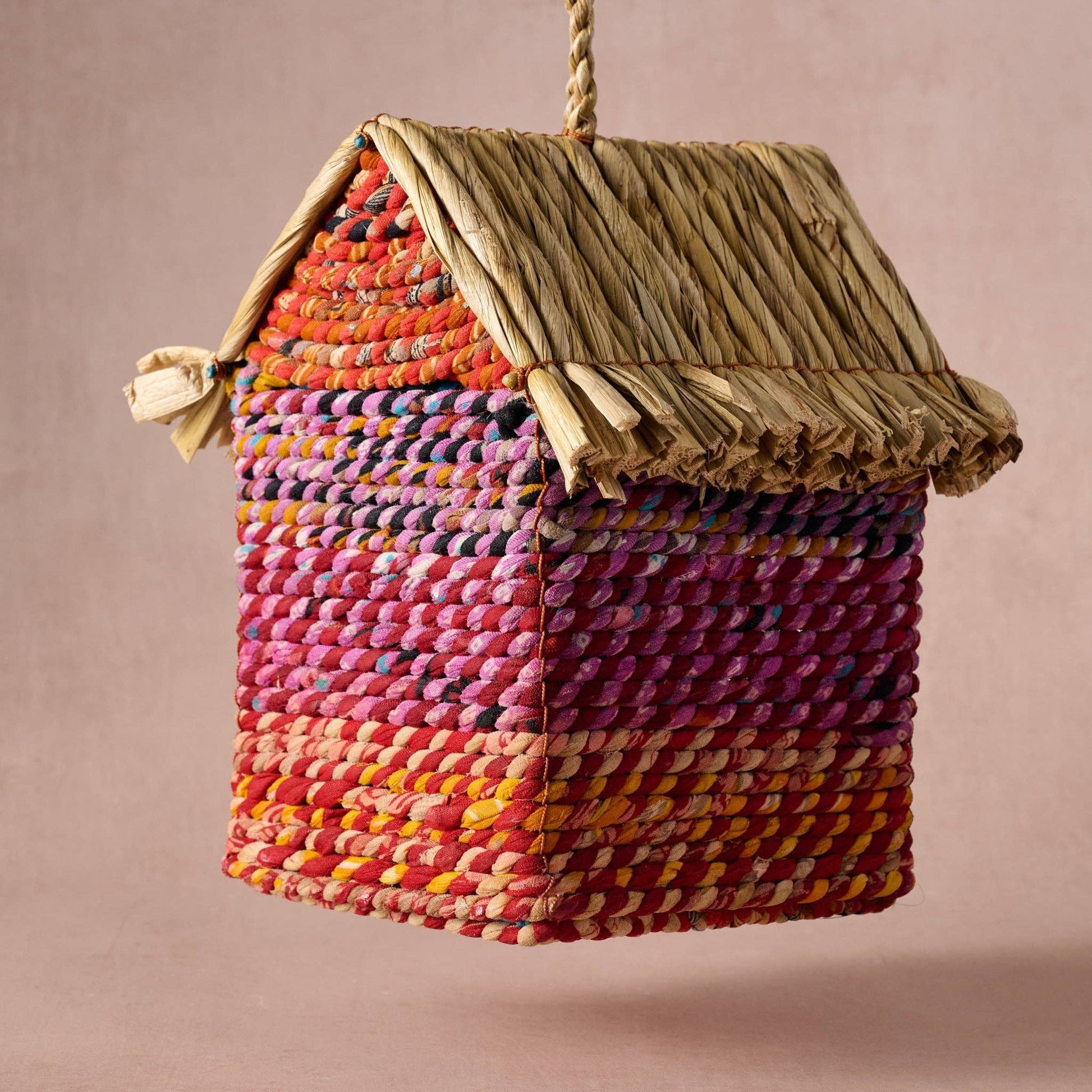 Colorful woven birdhouse hanging against a beige background