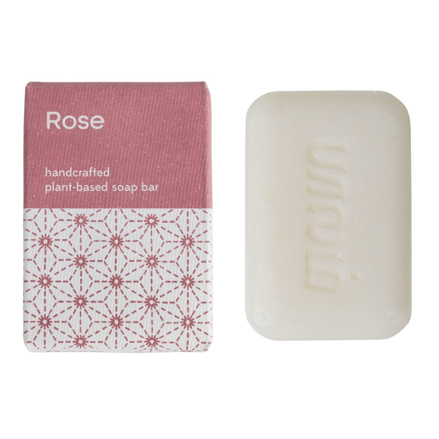 A bar of soap with a pink and white label that reads 'rose' and 'handcrafted plant-based soap bar' with a geometric pattern. The packaging has a pink backdrop and a white border.