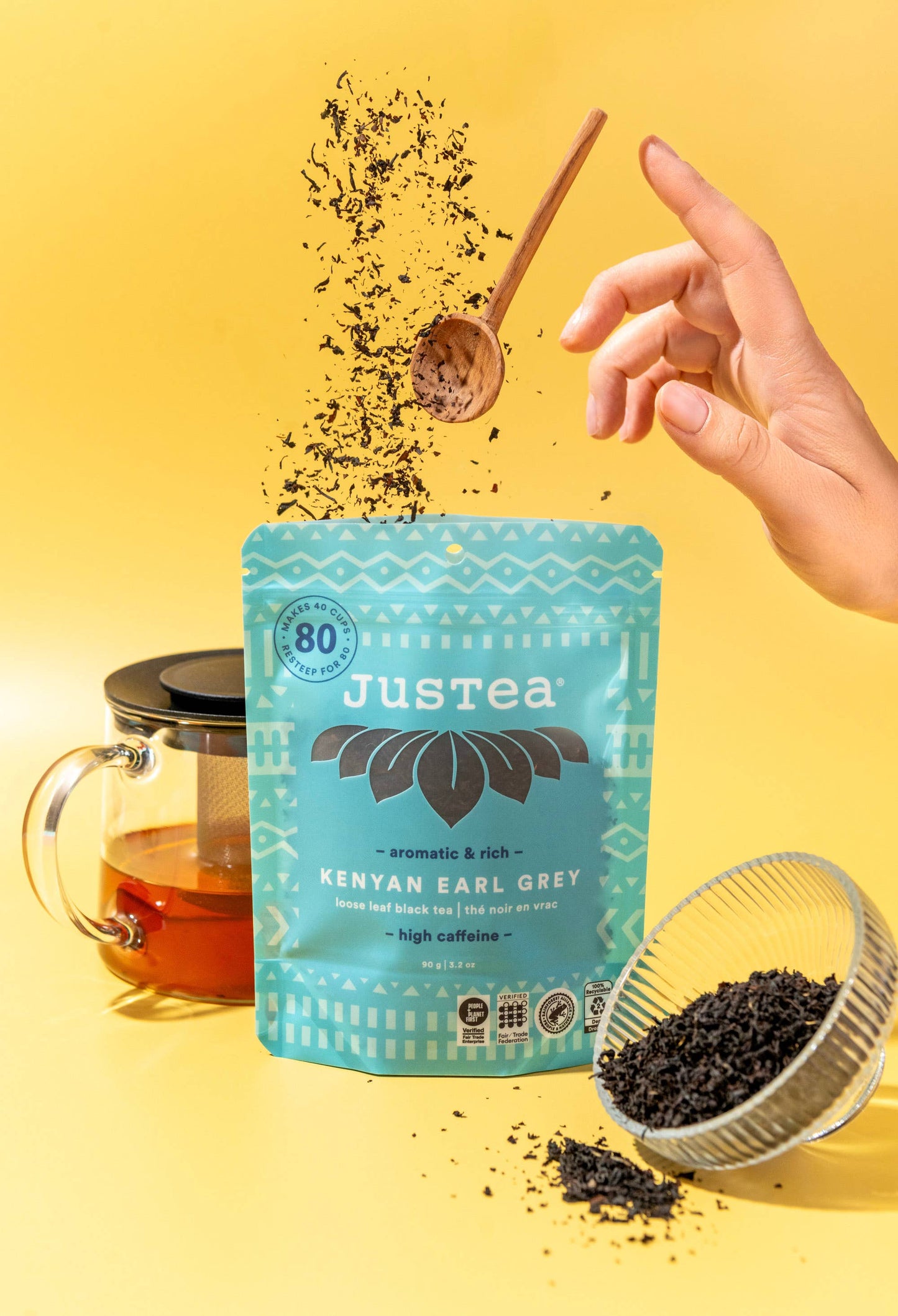 Justea tea packaging with a hand holding a spoon over it, yellow background