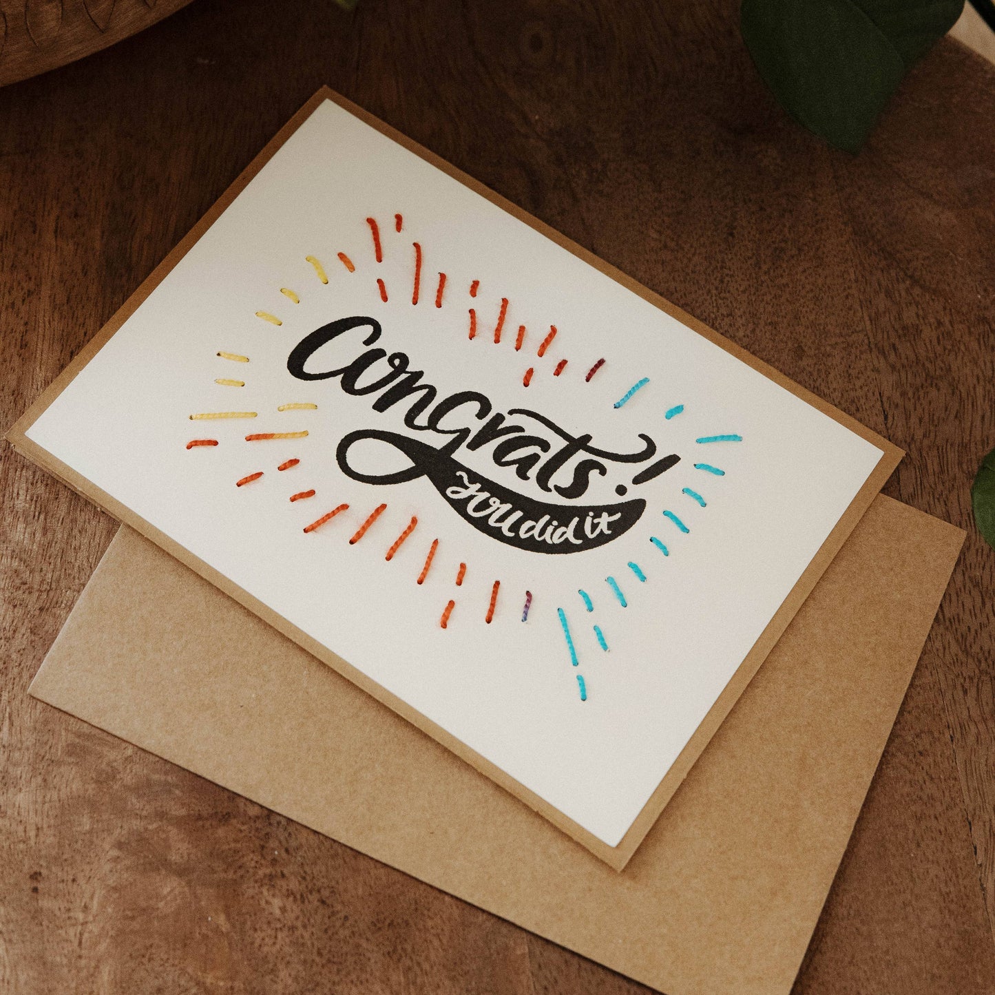 Greeting card with 'Congrats' text on a wooden surface with a plant in the background