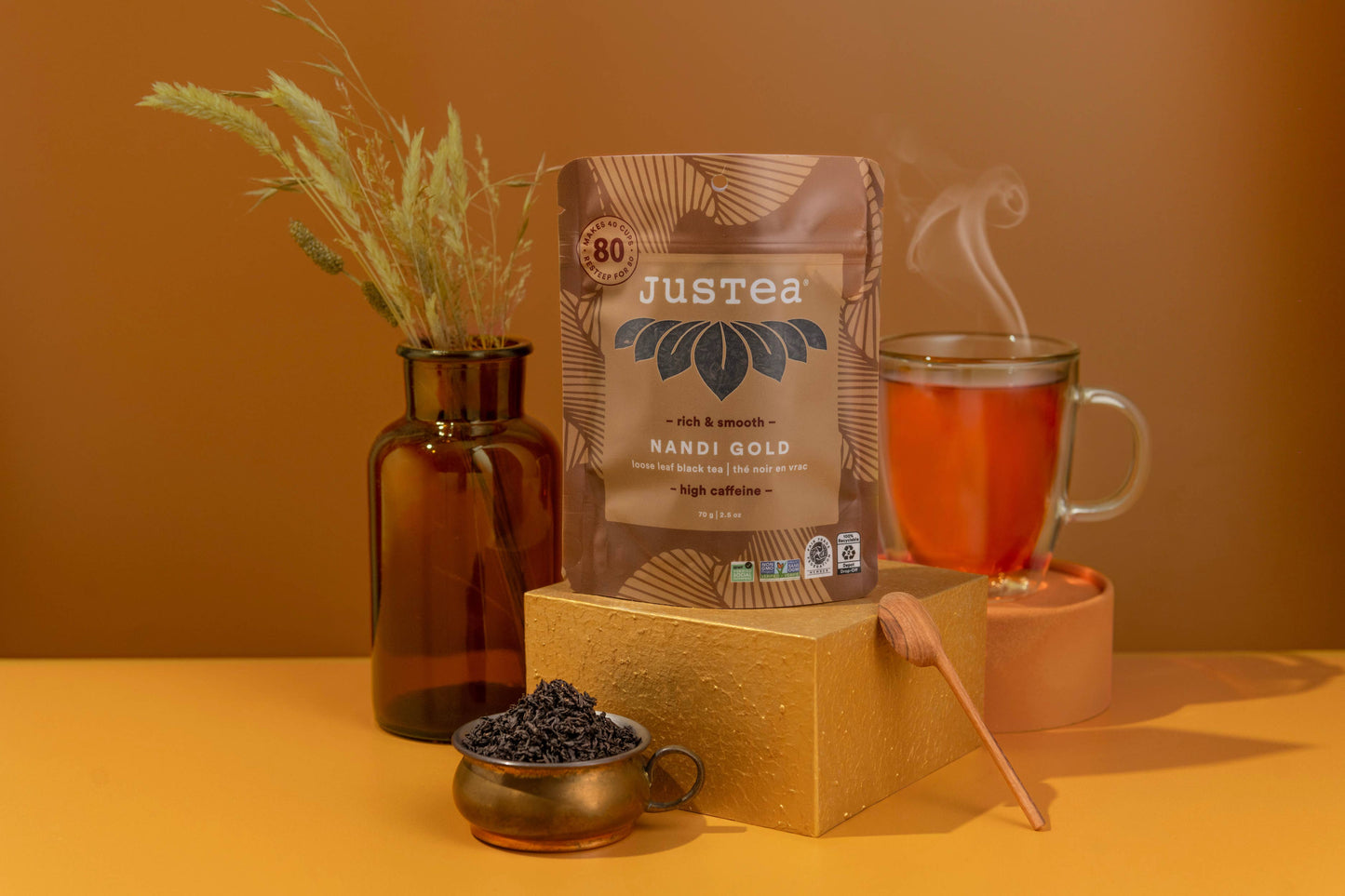 Justea Nandi Gold coffee package with a cup of coffee and coffee beans on a warm-toned background