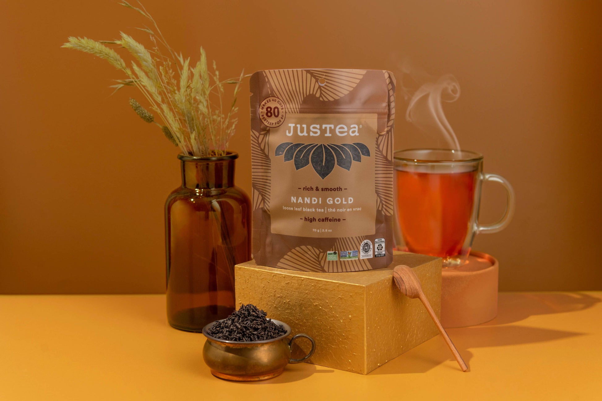 Justea Nandi Gold coffee package with a cup of coffee and coffee beans on a warm-toned background