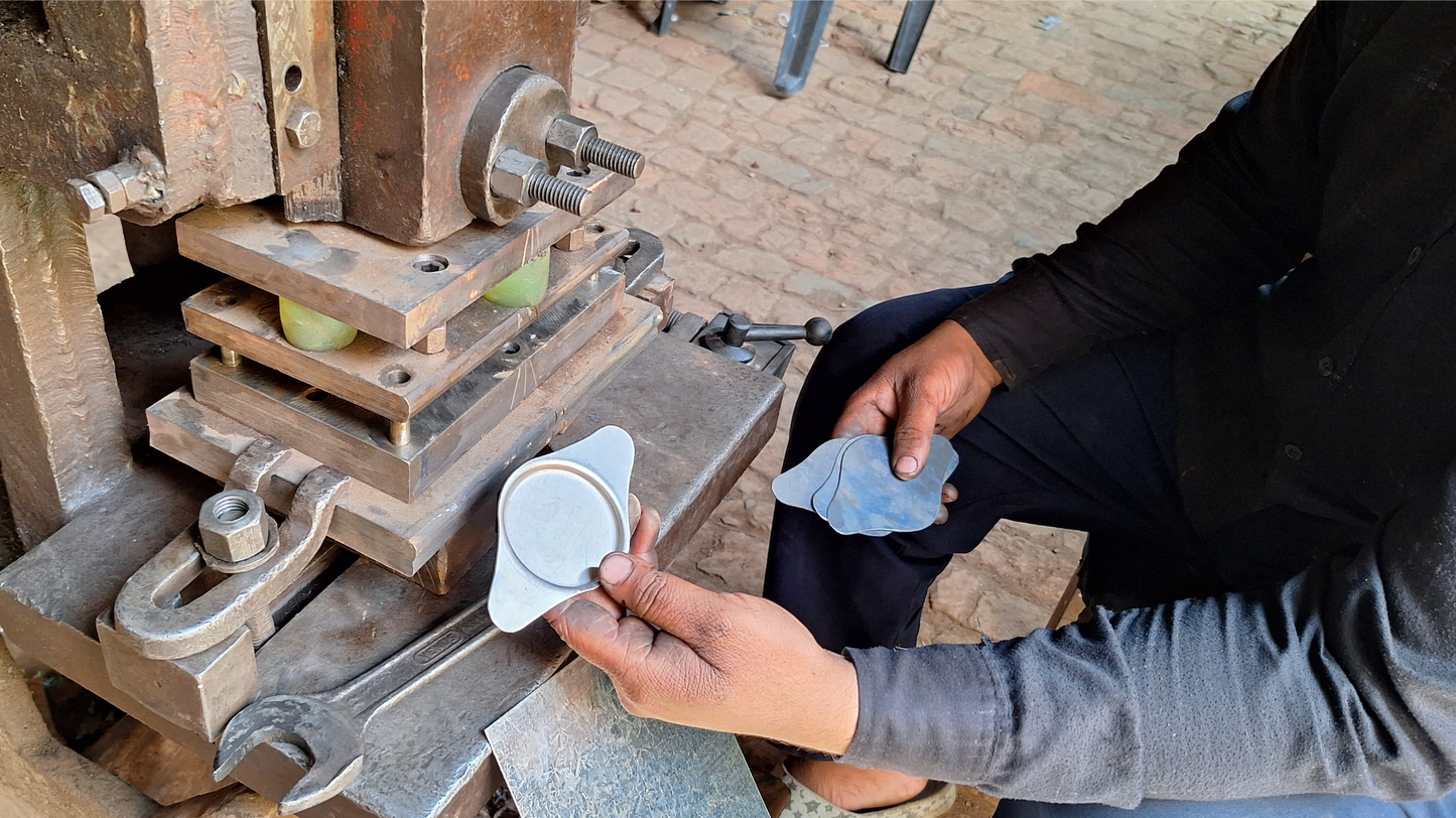 Person holding the tea tin lid/coaster next to the metal press machine that creates the indent in the metal. 