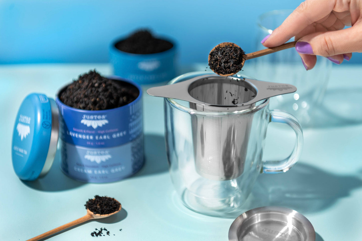 Person using a tea infuser with a container of tea leaves on a blue background
