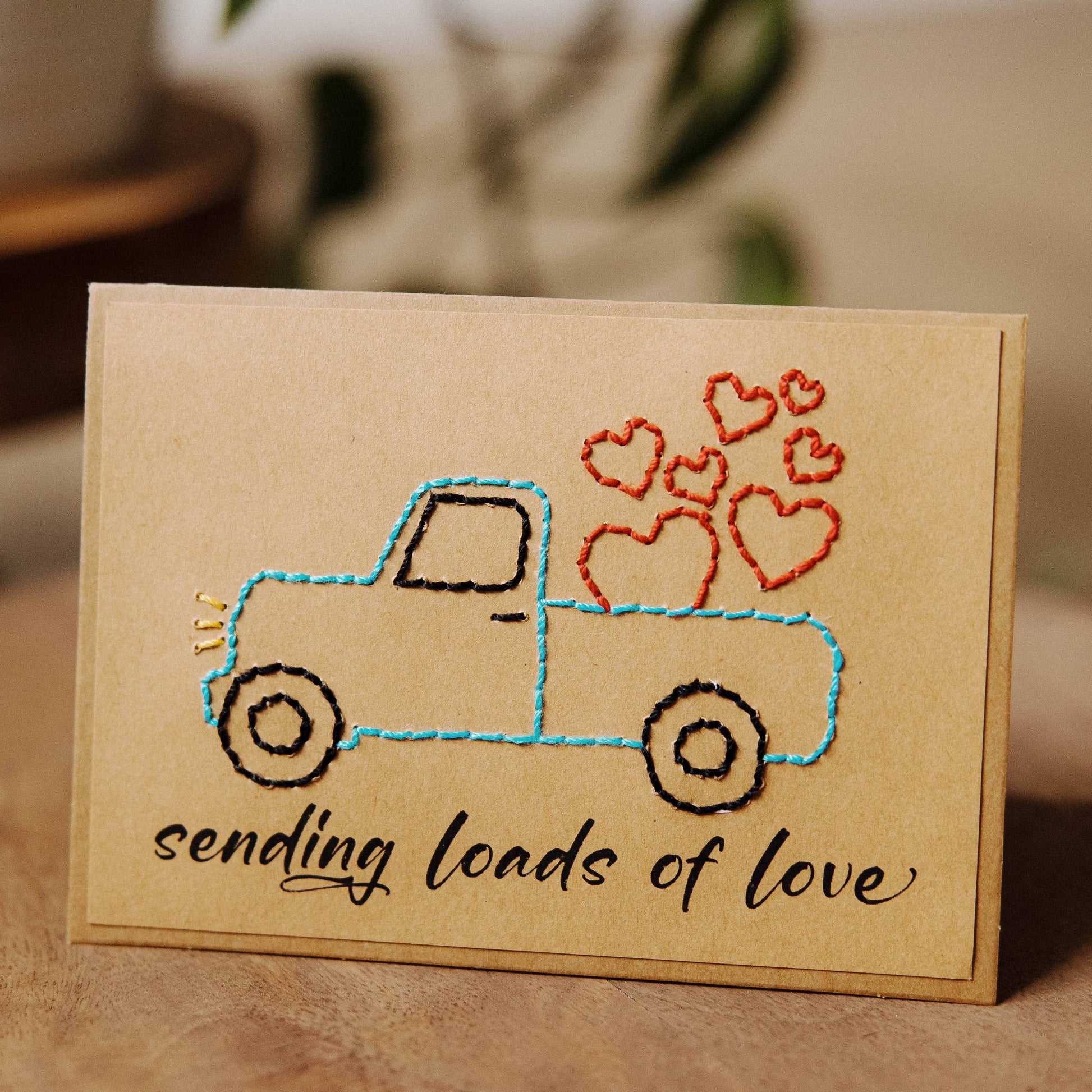 Card with embroidered truck and hearts design on a brown recycled paper surface