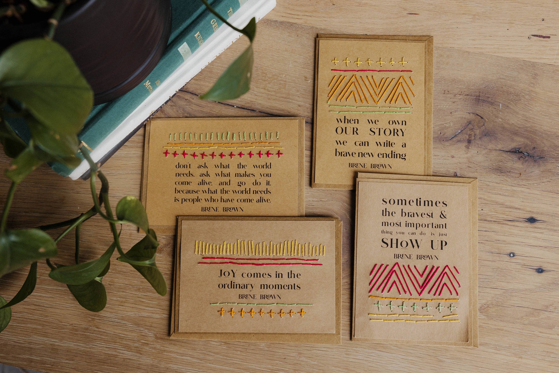 Four brown recycled paper cards with motivational quotes from Brene Brown styled on a wooden surface with a plant.