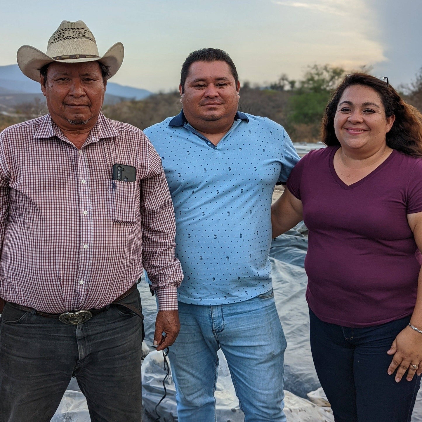 Three people standing together outdoors with a scenic background
