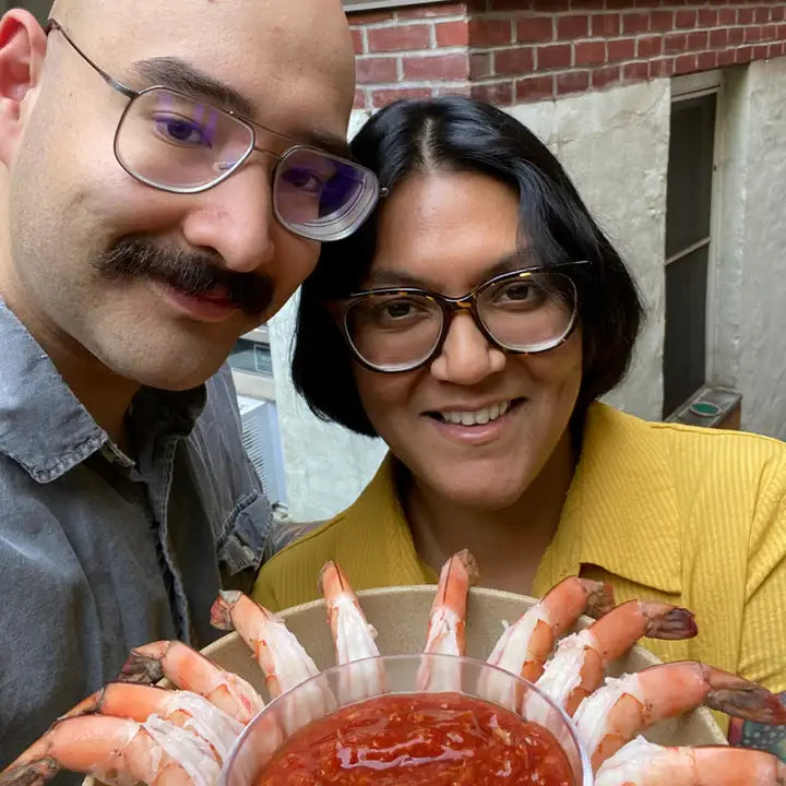 Two people holding a bowl of shrimp and sauce outdoors.