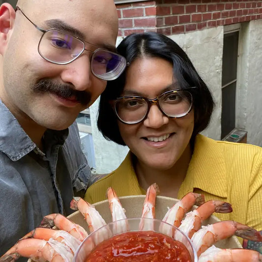 Two people holding a bowl of shrimp and sauce outdoors.