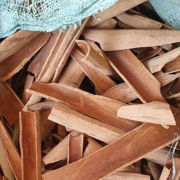 Stack of cinnamon bark with a green mesh bag in the background