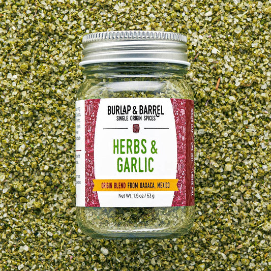 Jar of Burlap & Barrel Herbs & Garlic blend on a textured green background