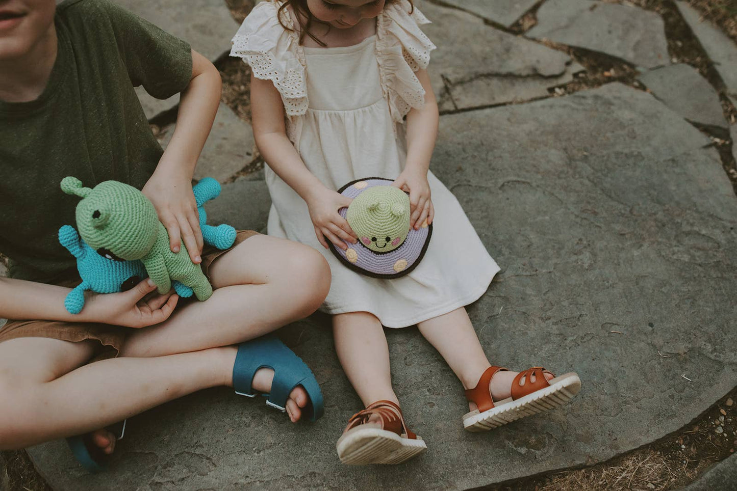 Two children sitting on a stone surface holding space themed stuffed toys.