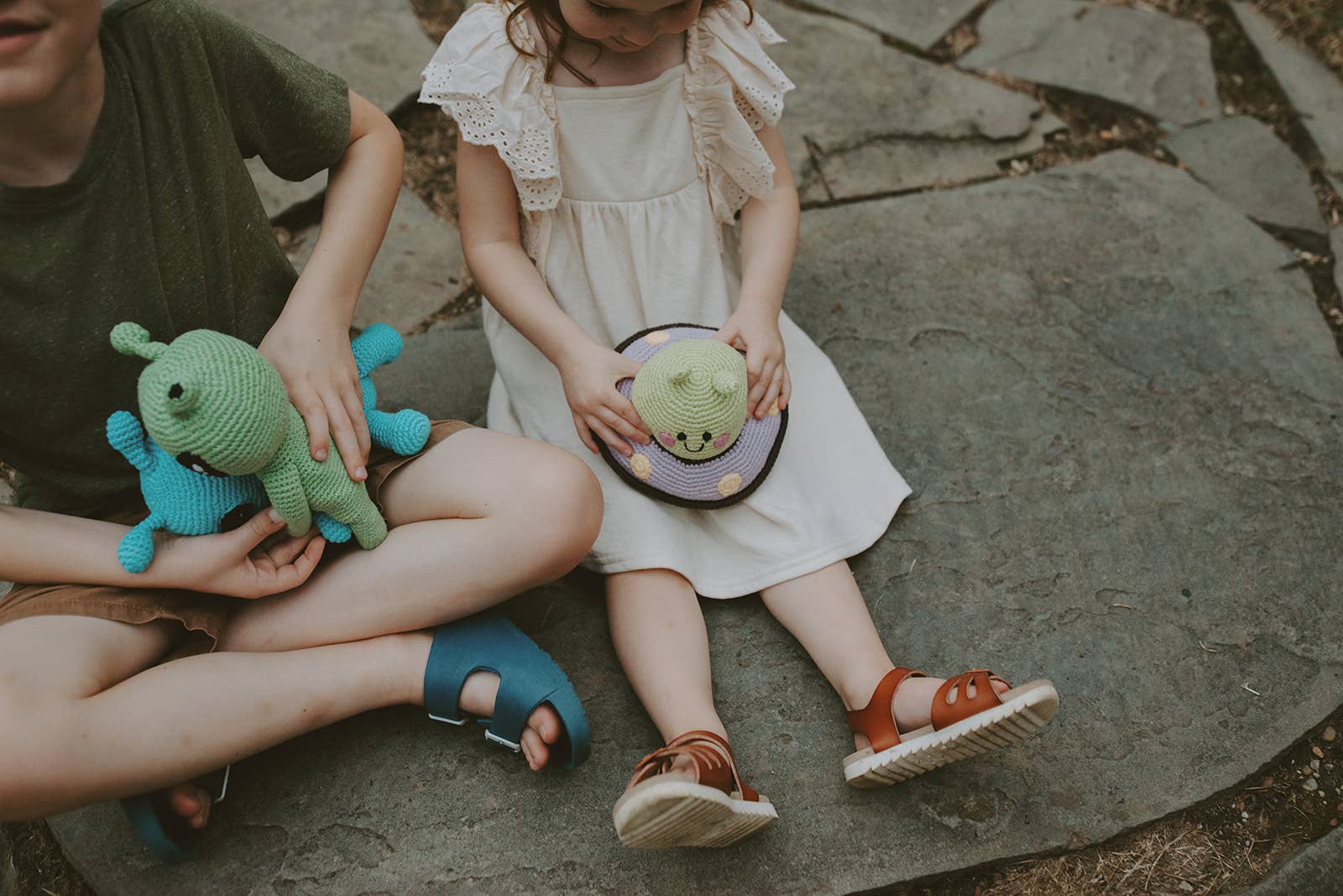 Two children sitting on a stone surface holding space themed stuffed toys.