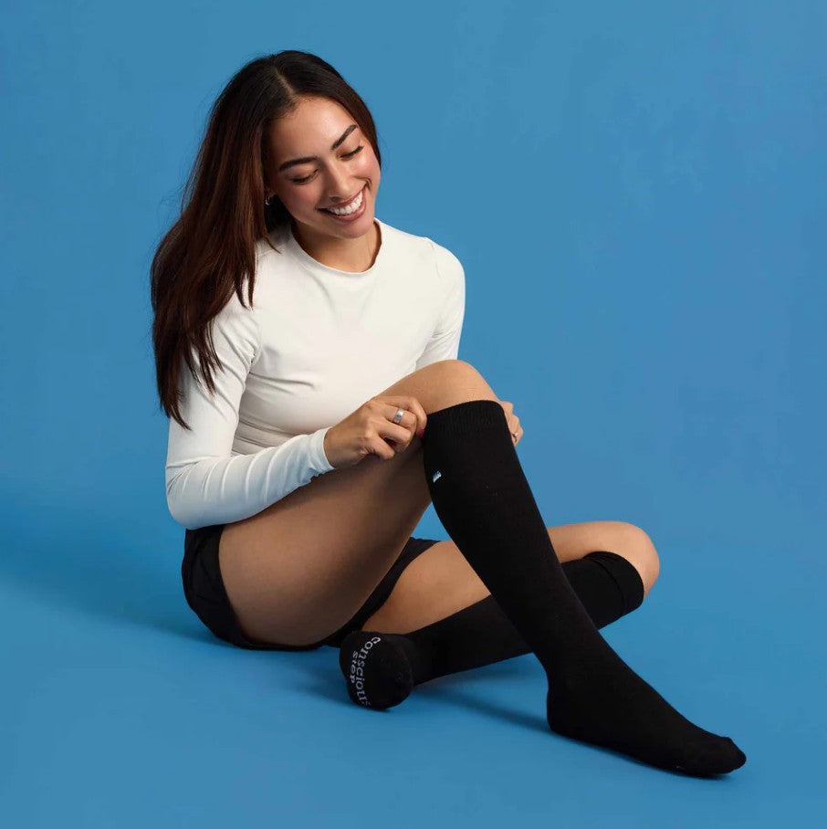 Woman sitting on a blue background wearing black knee-high socks.