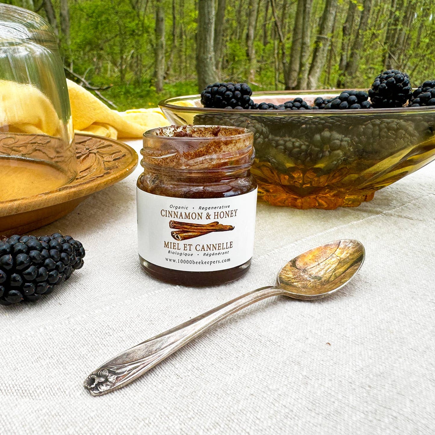 Jar of cinnamon honey with a spoon and blackberries on a table outdoors.