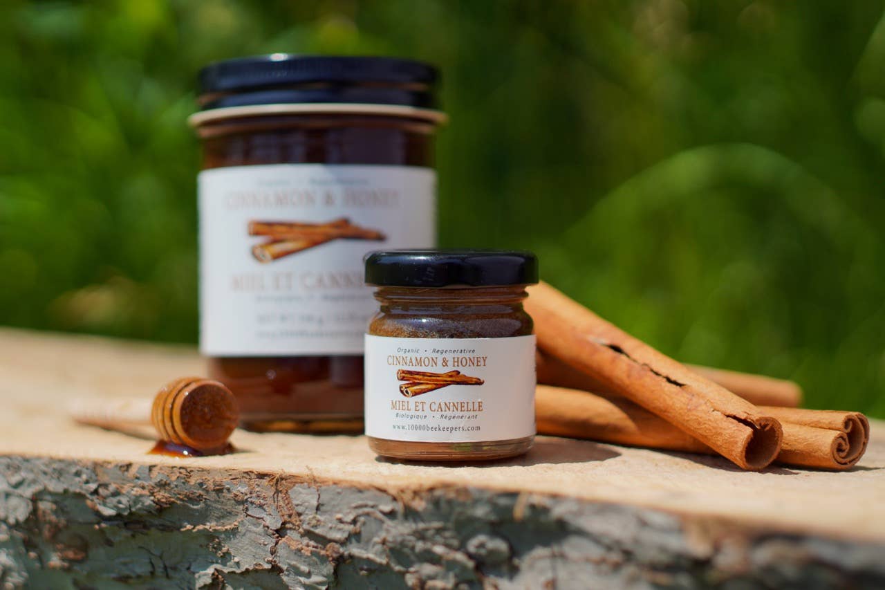 Two jars of cinnamon and honey spread on a wooden surface with cinnamon sticks in the background.