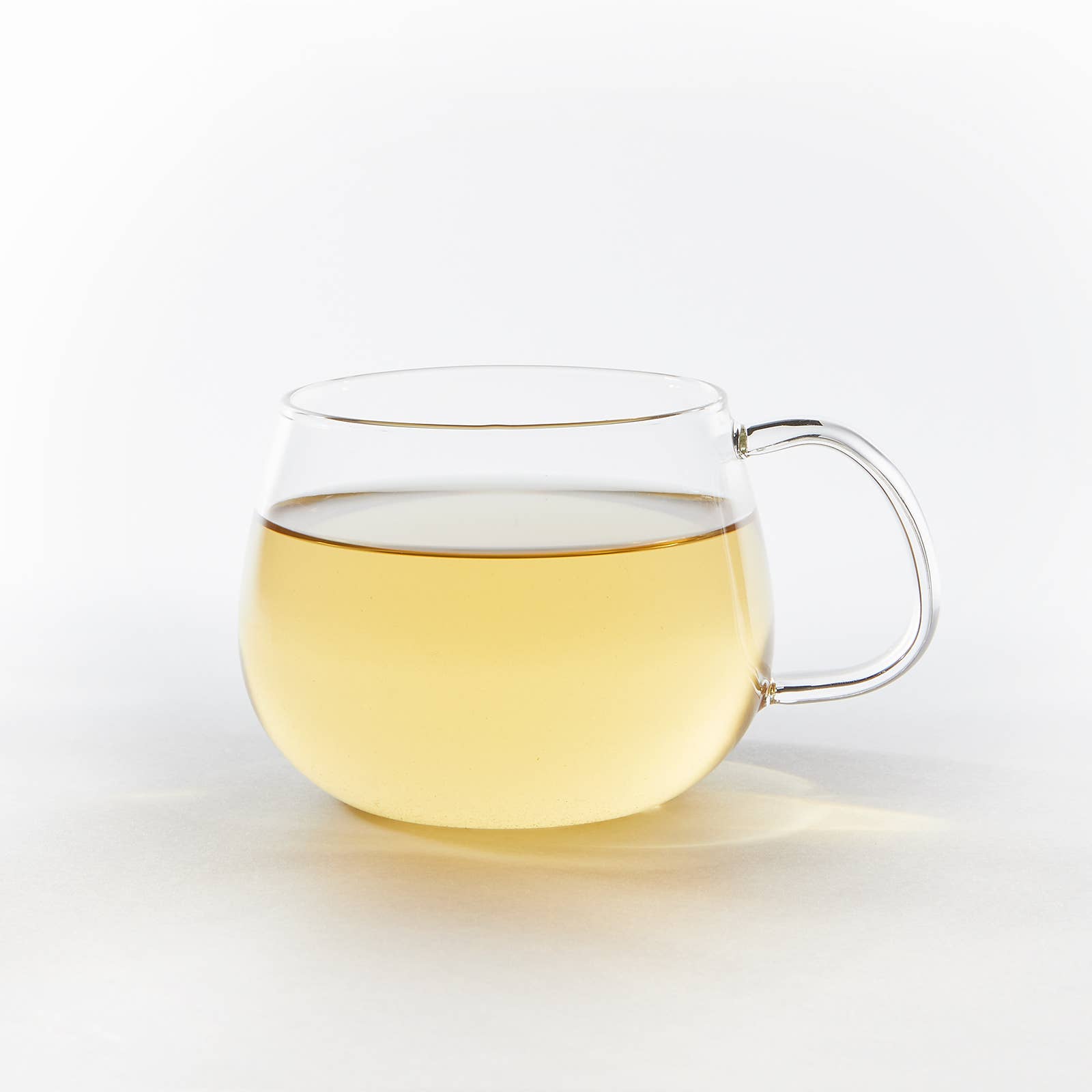 Clear glass mug with a handle filled with a pale yellow liquid on a white background
