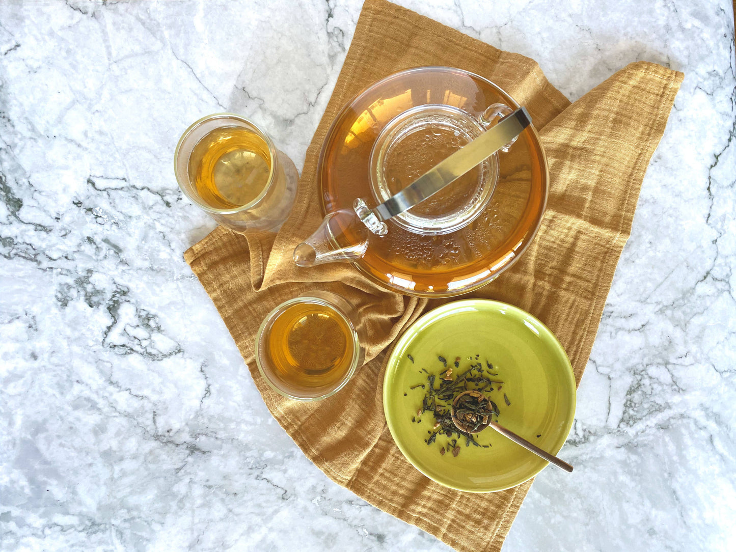 Tea-making setup with teapot, cups, and a bowl of tea leaves on a yellow tea towel.