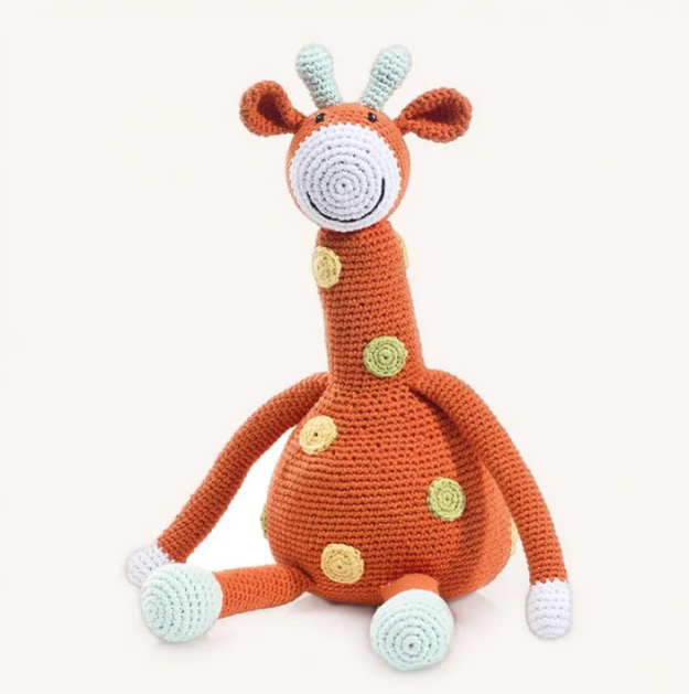 Crocheted giraffe toy with orange body, white face, and green accents on a white background